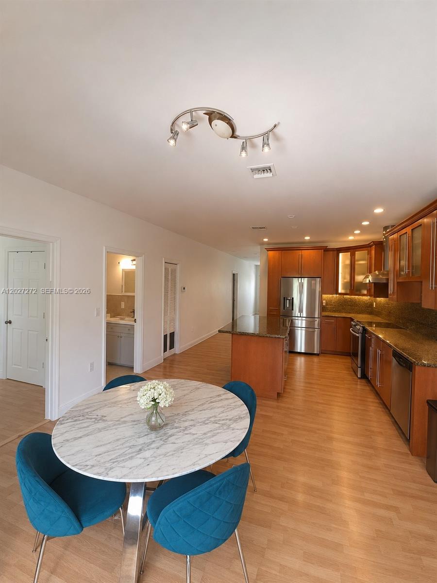 A kitchen with wood cabinets and a granite island opens to a dining area — 1101 NE 2nd St, Hallandale Beach FL 33009, HALLANDALE BEACH, FL