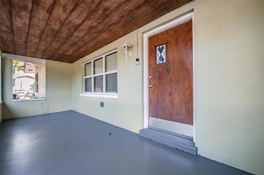 A covered porch features a wooden ceiling, a gray floor, and a wooden front door — 2025 PLAZA DOLORES, CLEARWATER, FL