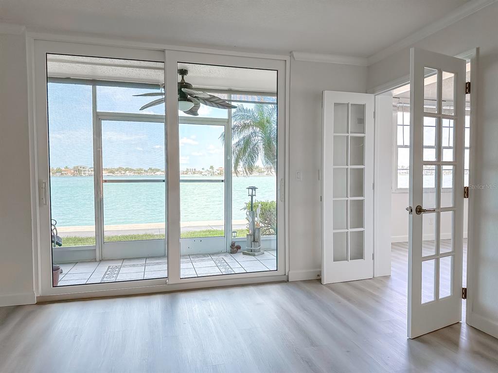 A room with light wood-look flooring features sliding glass doors opening to a waterfront patio — 7910 SUN ISLAND DRIVE S UNIT 101, SOUTH PASADENA, FL