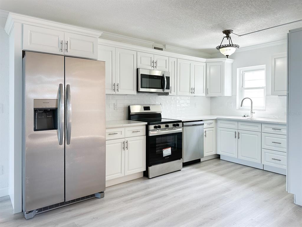 A kitchen features white cabinetry, stainless steel appliances, a subway tile backsplash, and light flooring — 7910 SUN ISLAND DRIVE S UNIT 101, SOUTH PASADENA, FL