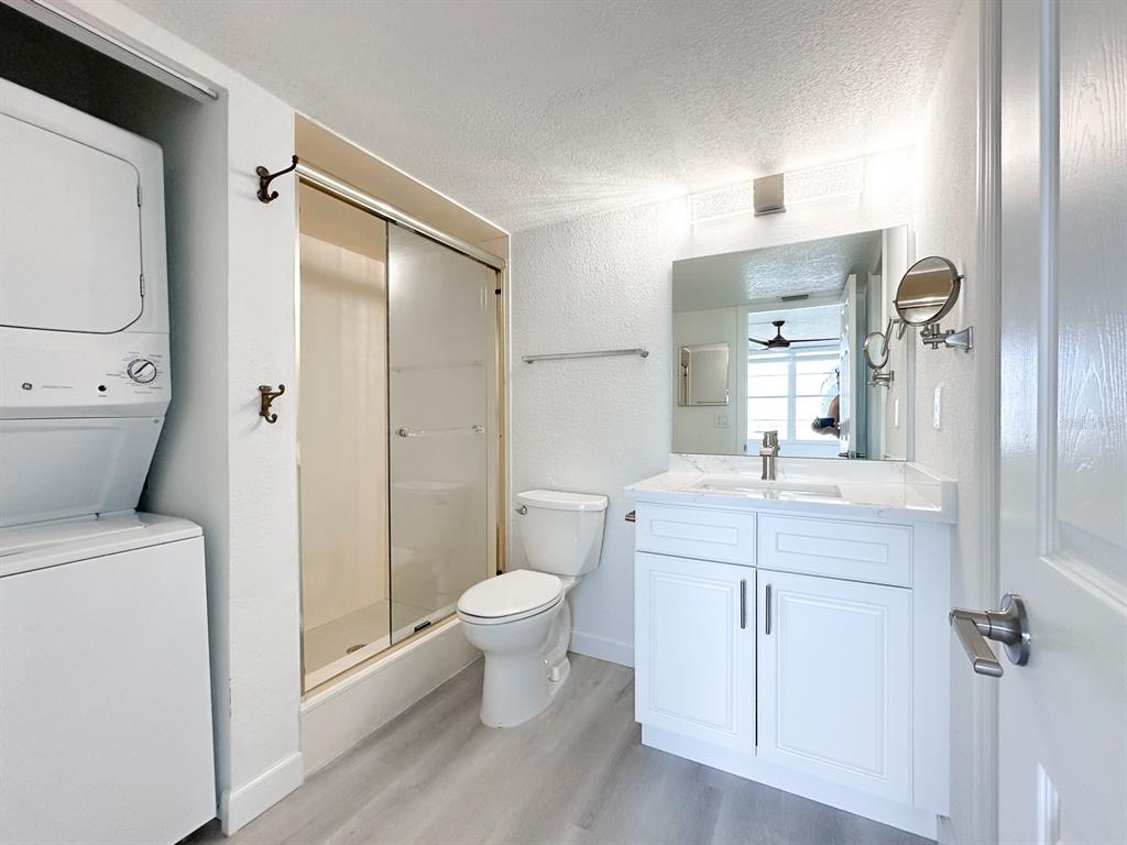 A bathroom features a stacked washer and dryer, a glass-enclosed shower, and a white vanity — 7910 SUN ISLAND DRIVE S UNIT 101, SOUTH PASADENA, FL