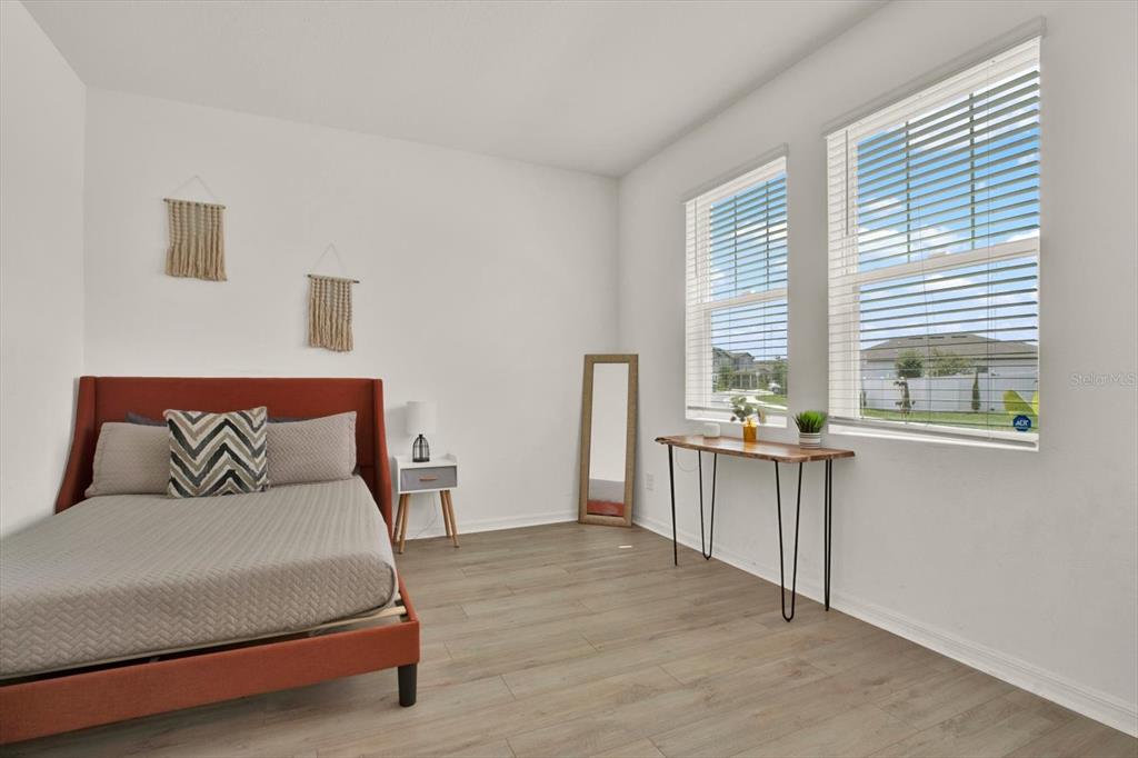 A bedroom features a rust-colored bed, wood-look flooring, a console table, and two large windows — 2310 LANCASHIRE STREET, DAVENPORT, FL