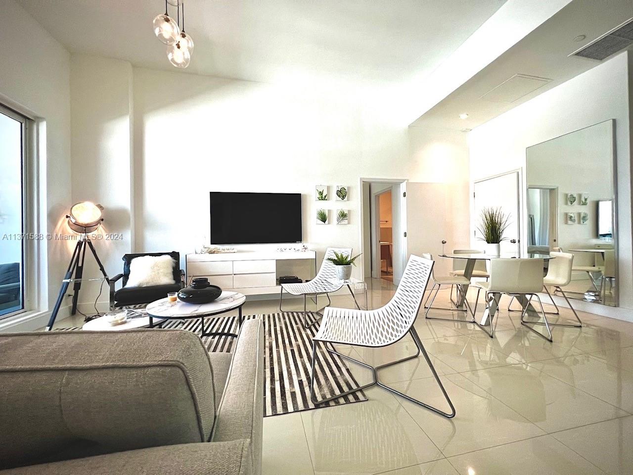 A bright, modern living and dining area features white tile floors and a striped rug — 2301 Collins Ave # 1626, Miami Beach FL 33139, MIAMI BEACH, FL