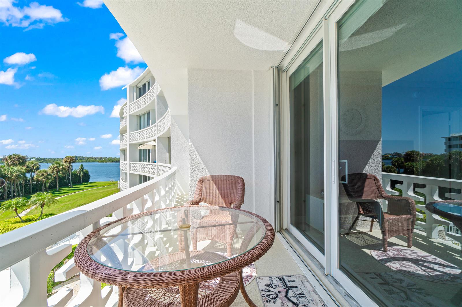 A balcony with wicker furniture overlooks a grassy lawn, palm trees, and a body of water — 2760 S Ocean Boulevard # 313, Palm Beach FL 33480, PALM BEACH, FL