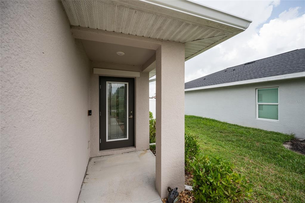 A covered entryway features a dark glass-paneled front door and a concrete porch floor — 137 HERCULES DRIVE, ROTONDA WEST, FL