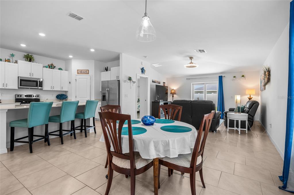 An open-concept kitchen and dining area features white cabinetry, teal bar stools, and tile flooring — 137 HERCULES DRIVE, ROTONDA WEST, FL