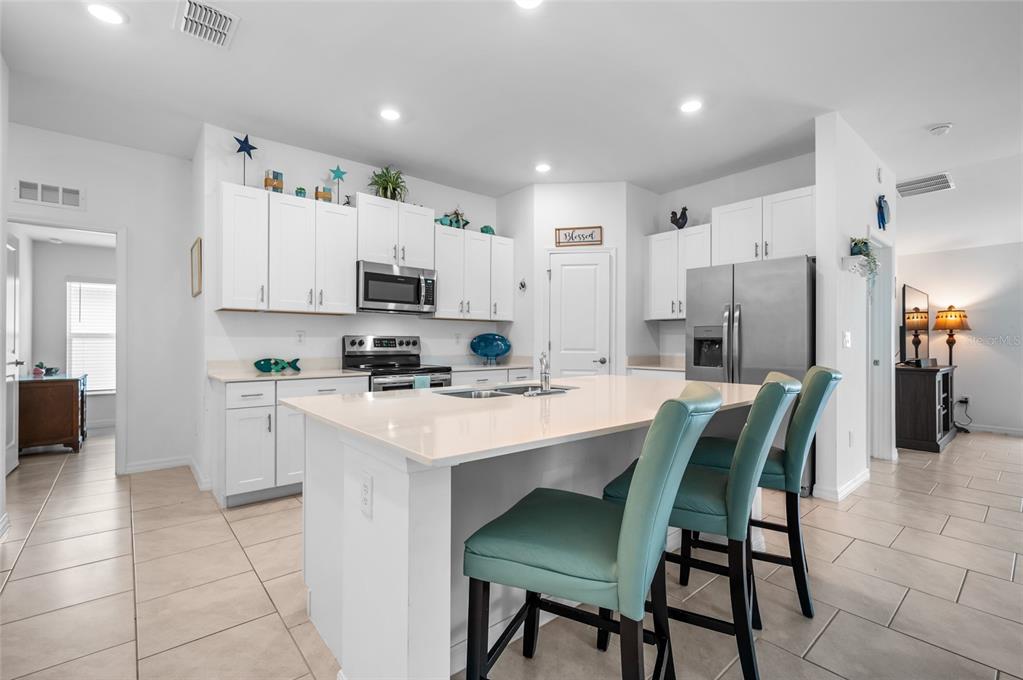 A kitchen features white cabinets, stainless steel appliances, a quartz island, and teal bar stools — 137 HERCULES DRIVE, ROTONDA WEST, FL