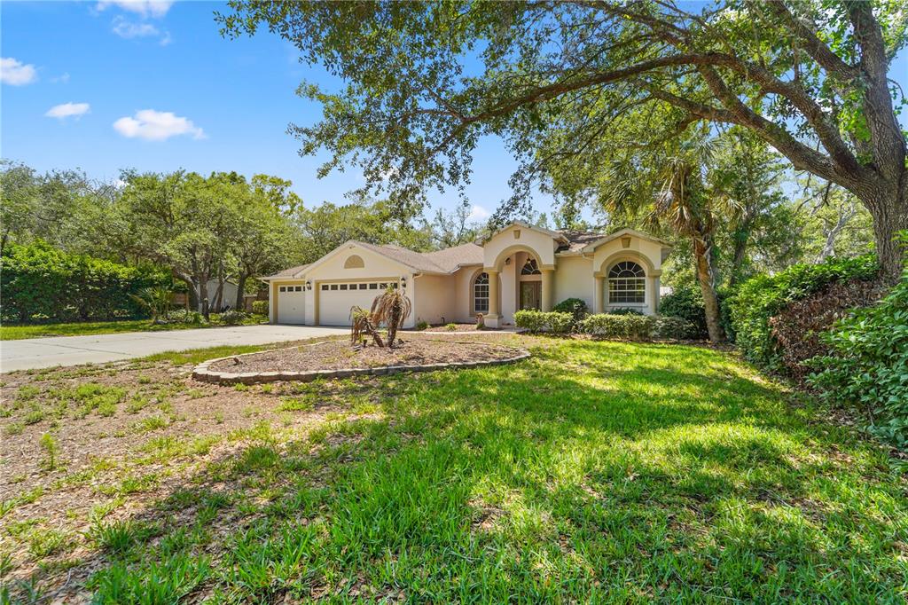 A single-story house with a two-car garage, arched entryway, and large trees in the yard — 9183 NIGHTINGALE ROAD, WEEKI WACHEE, FL