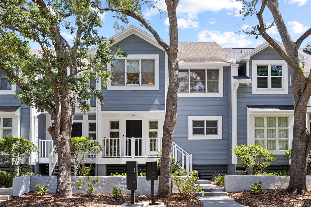 A blue-sided townhouse exterior features a front porch, white trim, and mature trees — 4833 W FLAMINGO RD, TAMPA, FL