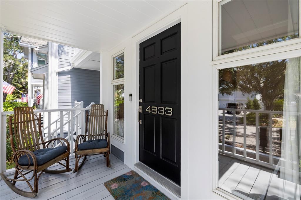 A front porch features two wooden rocking chairs, a black door, and white railings — 4833 W FLAMINGO RD, TAMPA, FL