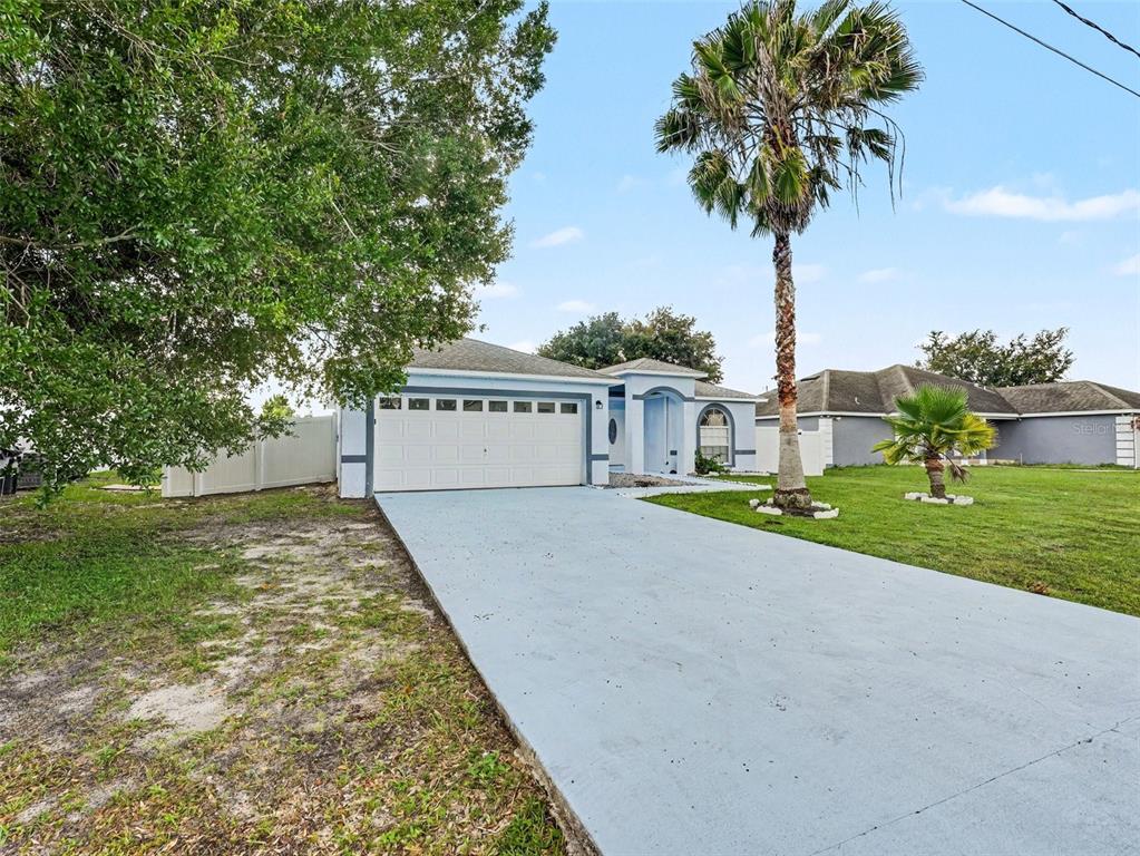 A single-story house with a blue-painted driveway, a two-car garage, and a tall palm tree — 645 LINNET COURT, POINCIANA, FL