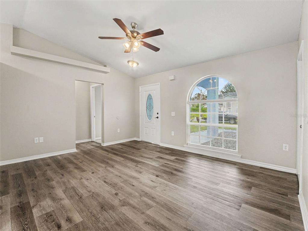 An empty room with wood-look flooring, a ceiling fan, a front door, and arched window — 645 LINNET COURT, POINCIANA, FL