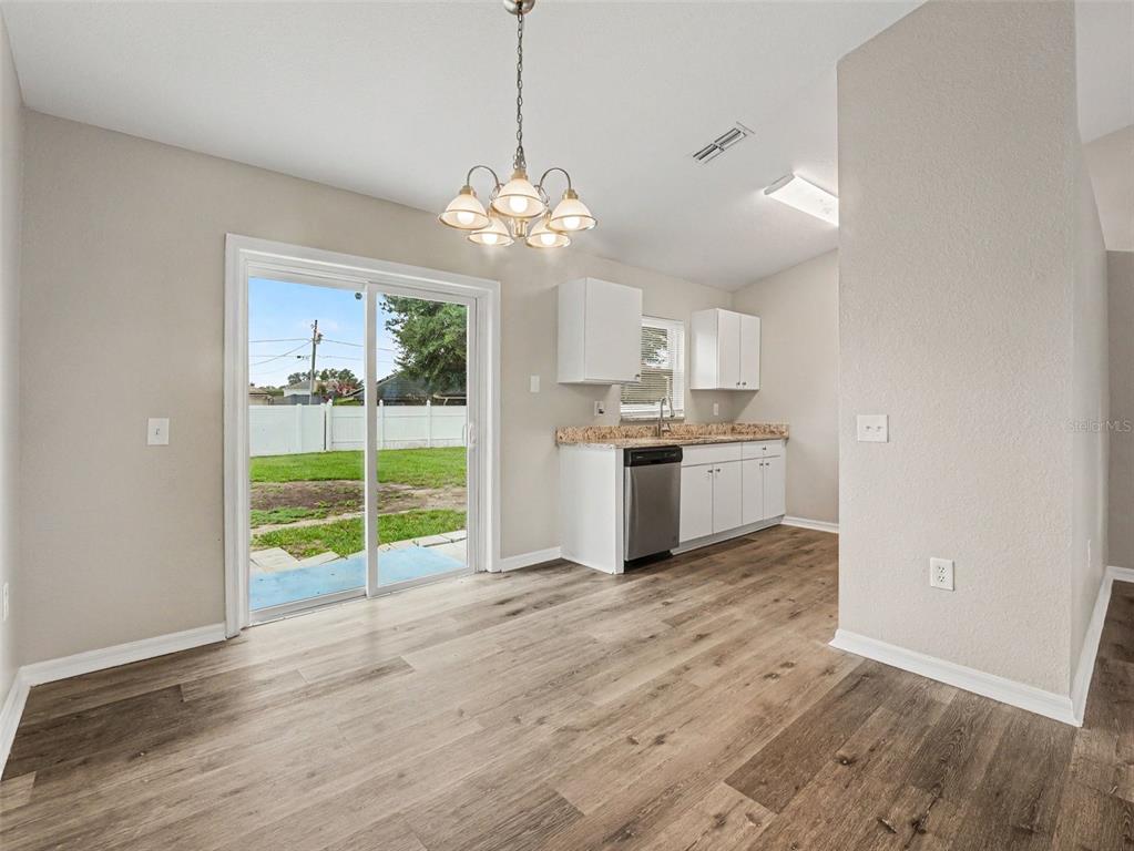 A dining area with wood-look flooring, a chandelier, and a sliding glass door to the yard — 645 LINNET COURT, POINCIANA, FL