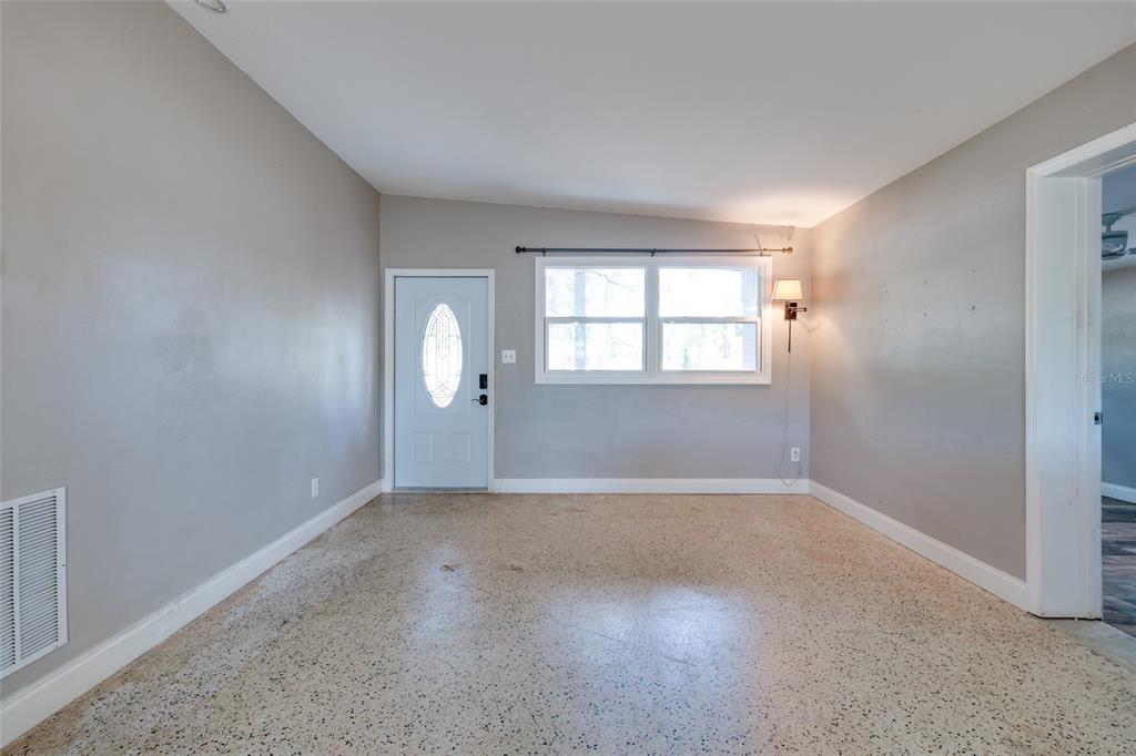 An empty room with gray walls, a white front door, and speckled terrazzo flooring — 5601 CEDAR STREET NE, ST PETERSBURG, FL