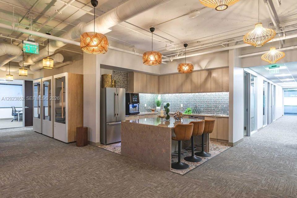 A modern office kitchen features a stone-topped island, bar stools, and hanging woven pendant lights — 515 N Flagler Dr, West Palm Beach FL 33401, WEST PALM BEACH, FL