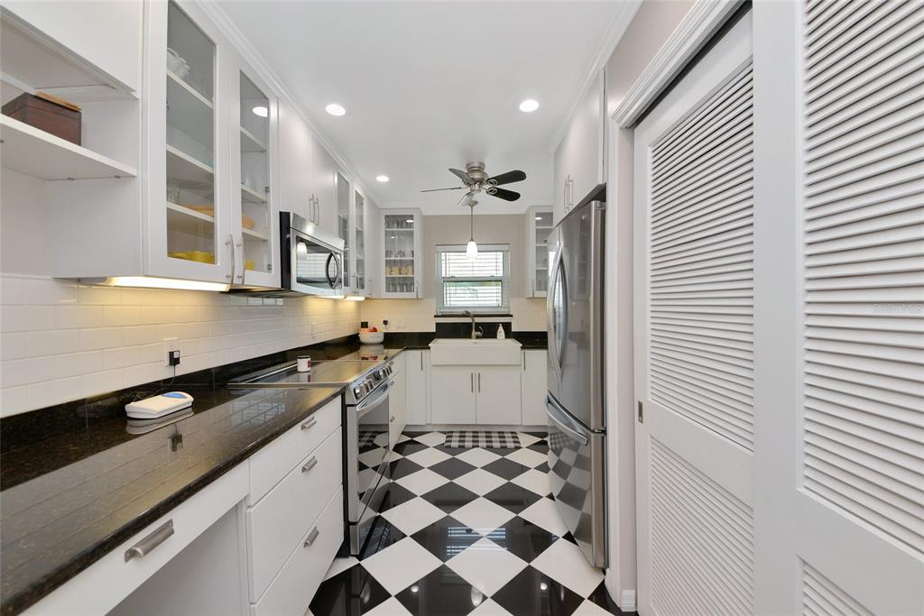 A galley kitchen features white cabinets, black countertops, and a black-and-white checkered tile floor — 6220 29TH AVENUE W UNIT 6220, BRADENTON, FL