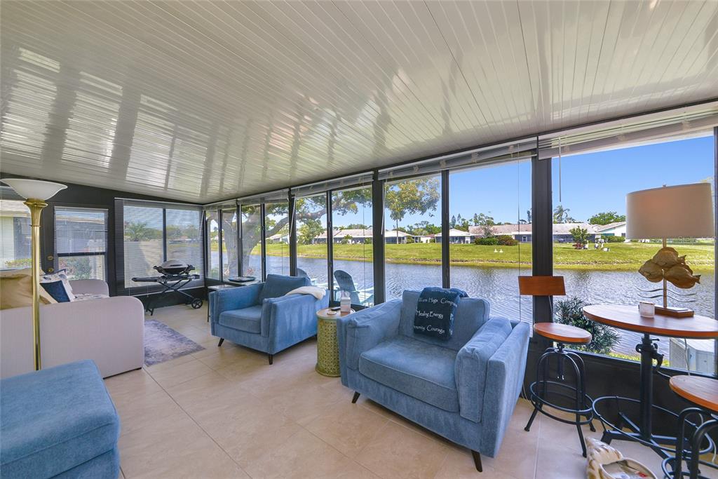A sunroom with tile floors features blue armchairs and large windows overlooking a pond — 6220 29TH AVENUE W UNIT 6220, BRADENTON, FL