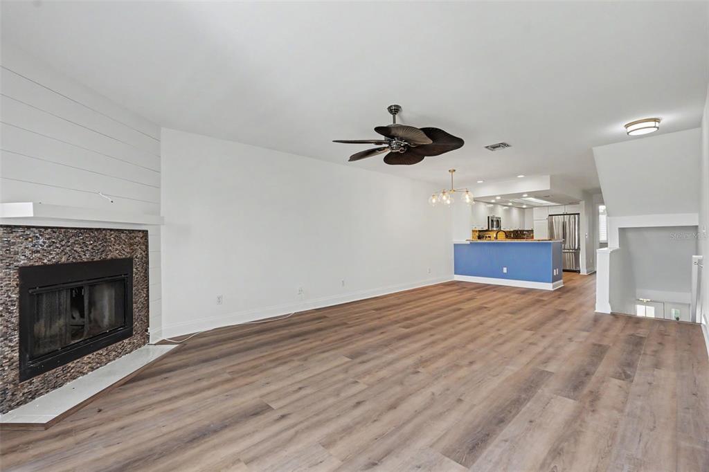 A living room with wood-look flooring, a stone fireplace, and an open kitchen beyond — 269 MADEIRA CIRCLE, ST PETERSBURG, FL