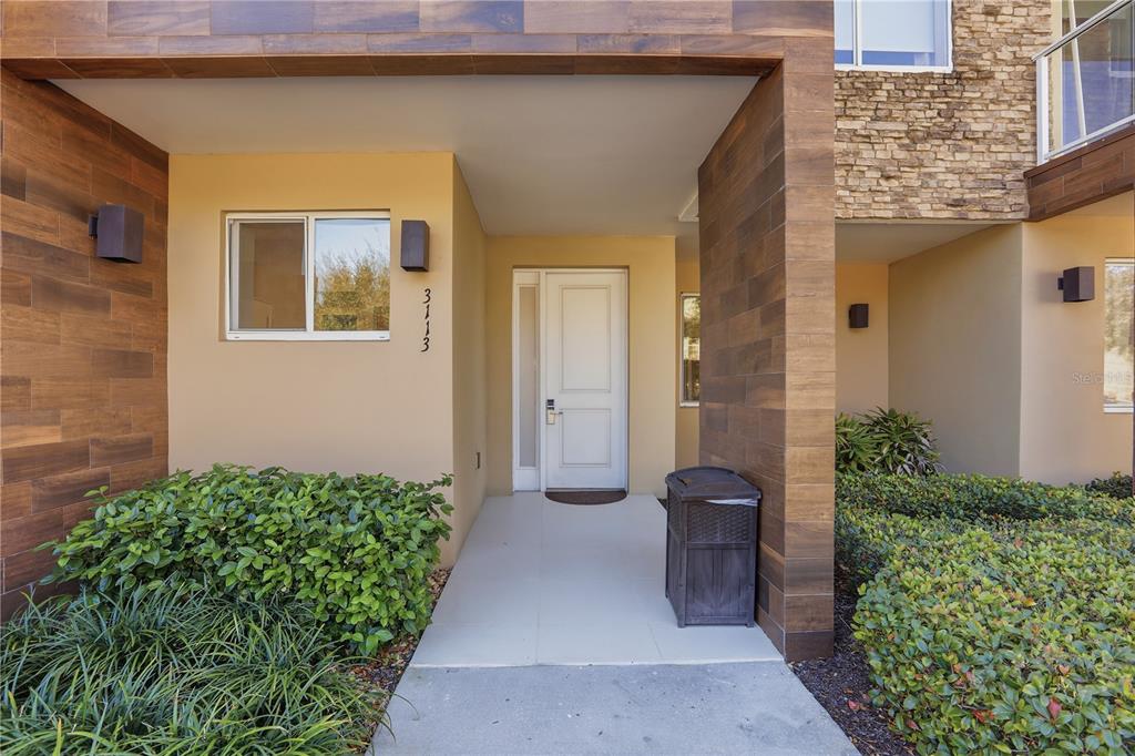 The exterior entrance features a white door, wood-look siding, and a small patch of landscaping — 3113 BRASILIA AVENUE, KISSIMMEE, FL