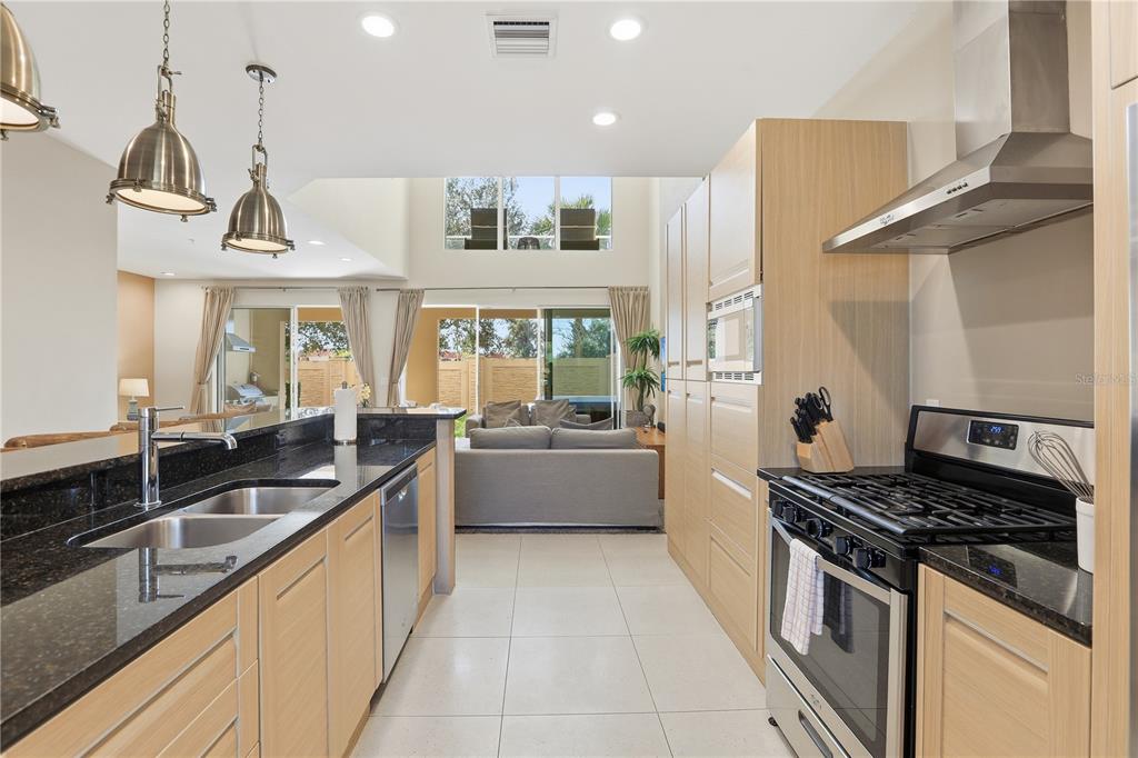 A modern kitchen with light wood cabinets, black granite countertops, and stainless steel appliances — 3113 BRASILIA AVENUE, KISSIMMEE, FL