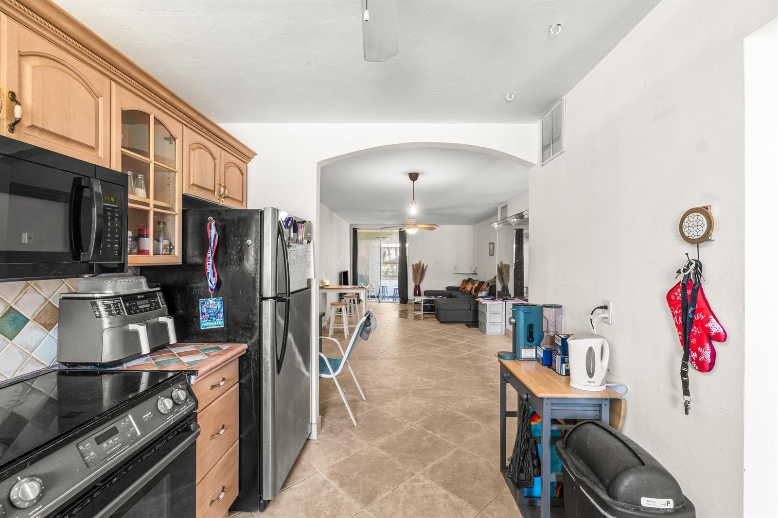A kitchen with wood cabinets and black appliances opens into a living area with tile floors — 750 SE 6th Avenue # 125, Deerfield Beach FL 33441, DEERFIELD BEACH, FL