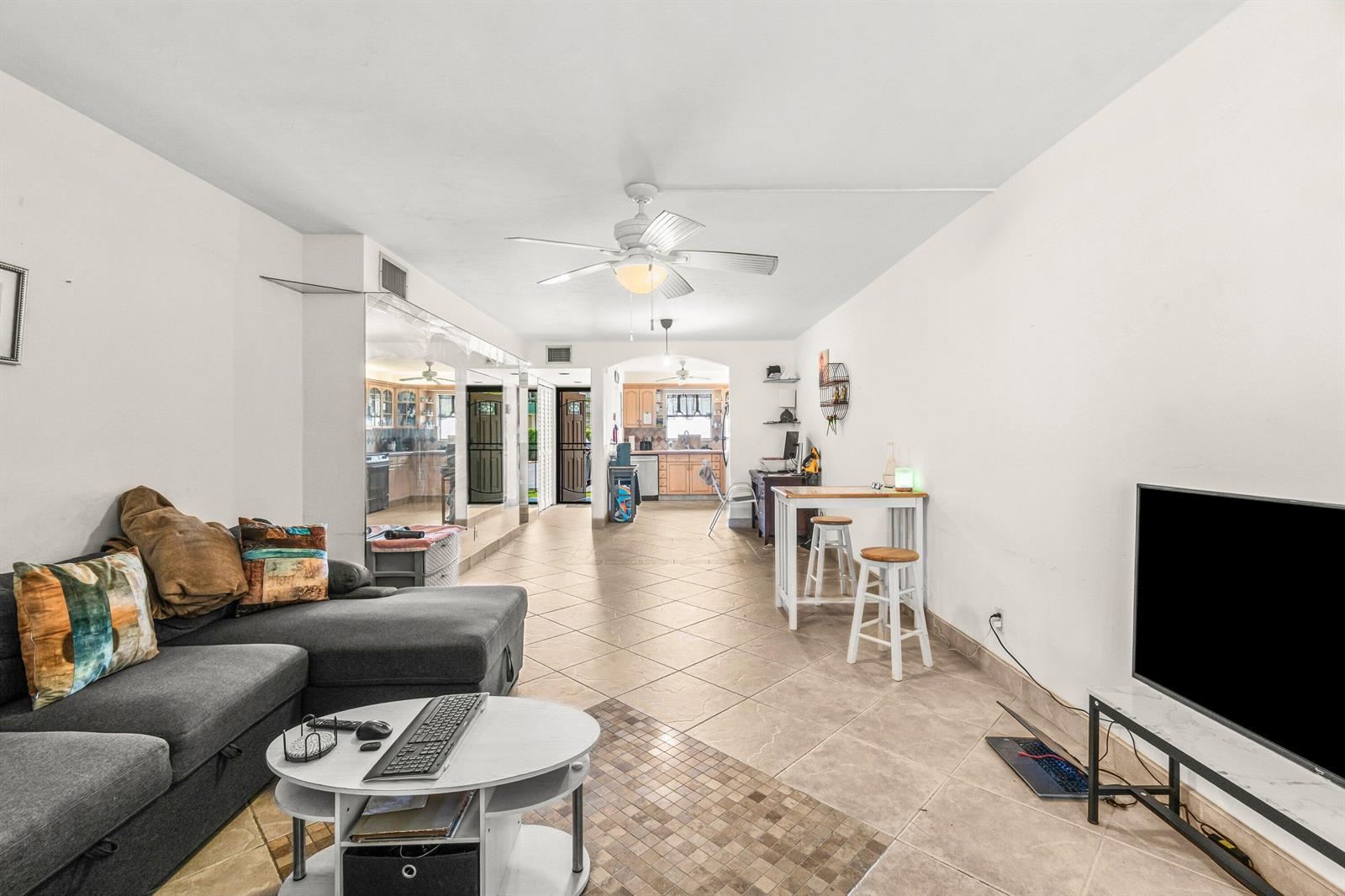 A living room with a grey sectional sofa, tile flooring, and an open kitchen beyond — 750 SE 6th Avenue # 125, Deerfield Beach FL 33441, DEERFIELD BEACH, FL