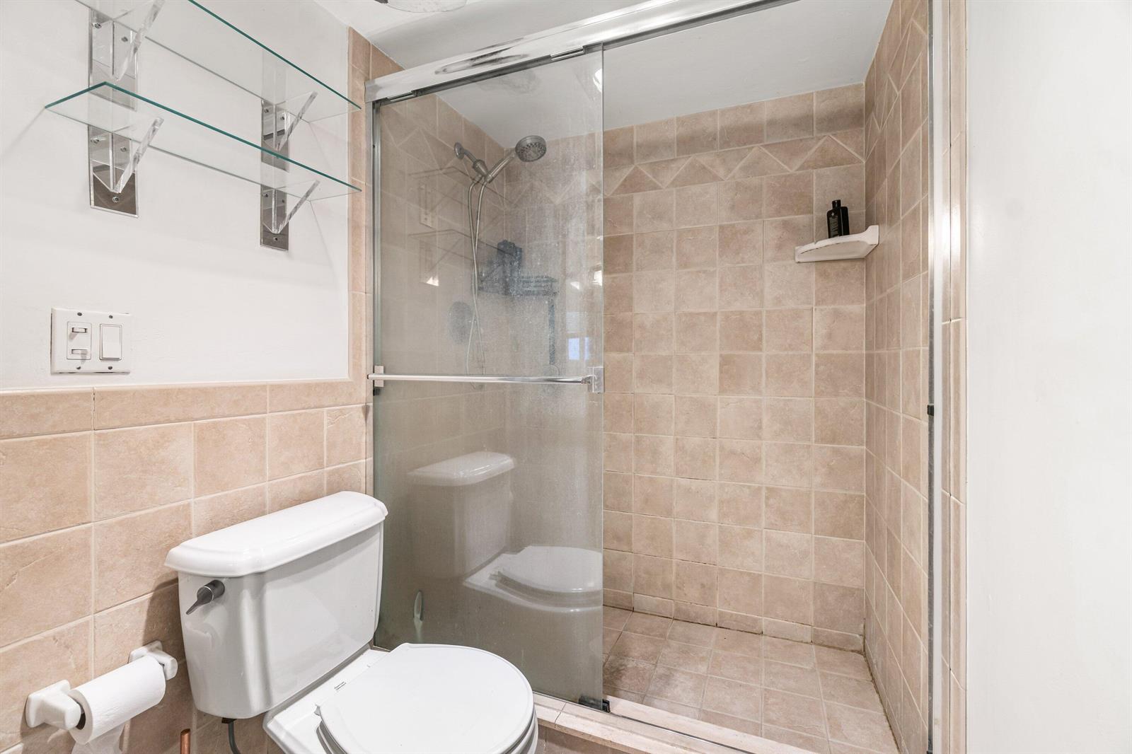 A bathroom features a glass-enclosed shower with tan tile walls next to a white toilet — 750 SE 6th Avenue # 125, Deerfield Beach FL 33441, DEERFIELD BEACH, FL