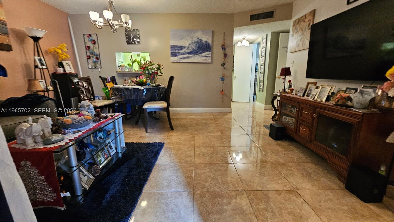 A living and dining area features tiled floors, a glass coffee table, and a television — 4980 E Sabal Palm Blvd # 132, Tamarac FL 33319, TAMARAC, FL