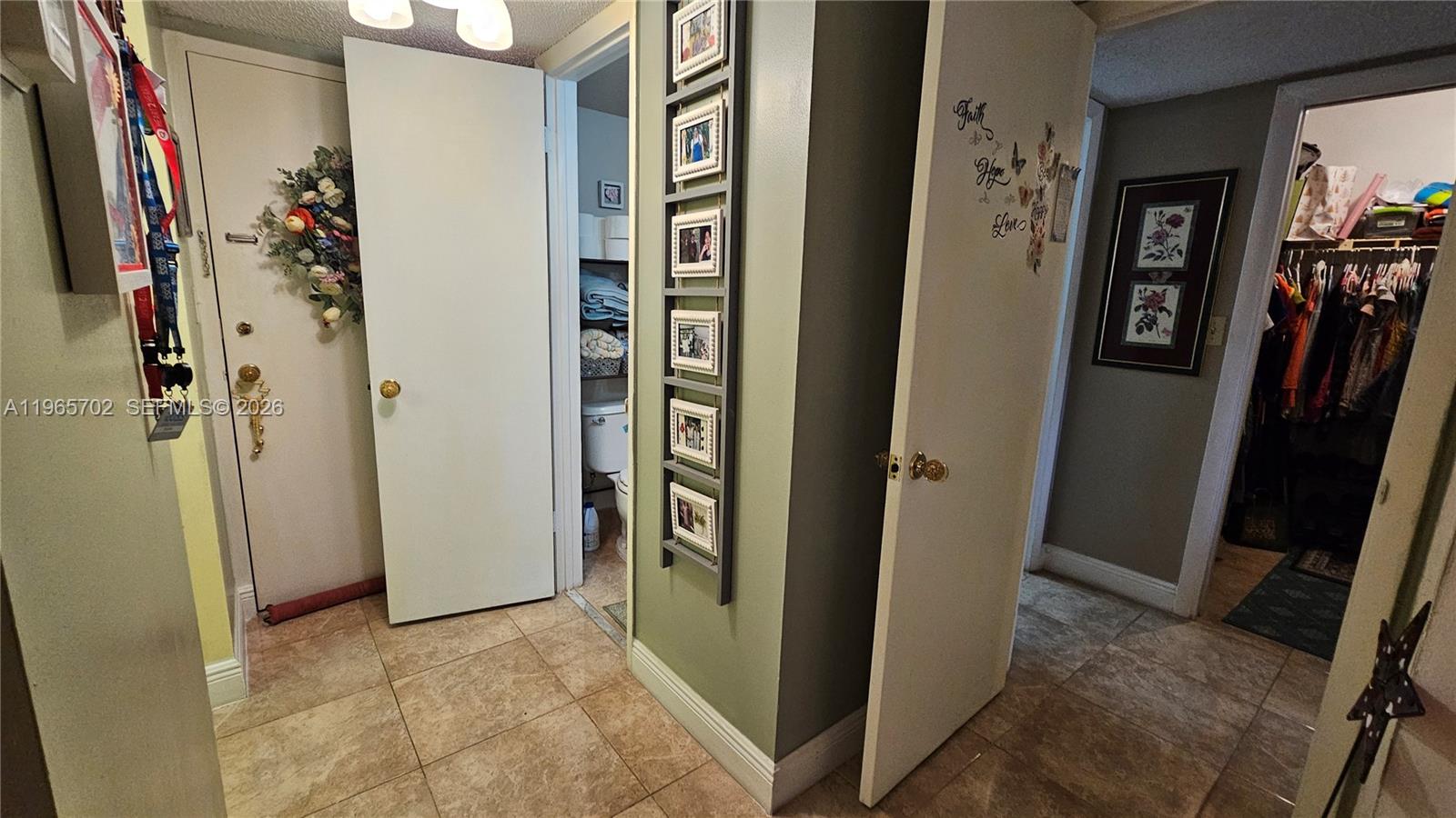 A hallway features tile flooring, a bathroom entrance, a wall-mounted photo display, and a closet — 4980 E Sabal Palm Blvd # 132, Tamarac FL 33319, TAMARAC, FL