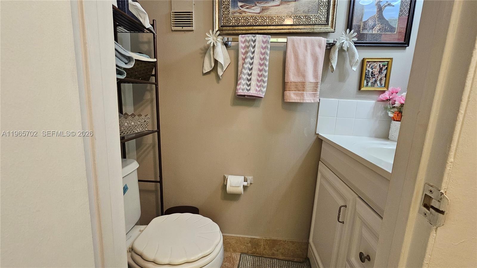 This small bathroom features a toilet, a vanity with a white cabinet, and wall-mounted towels — 4980 E Sabal Palm Blvd # 132, Tamarac FL 33319, TAMARAC, FL