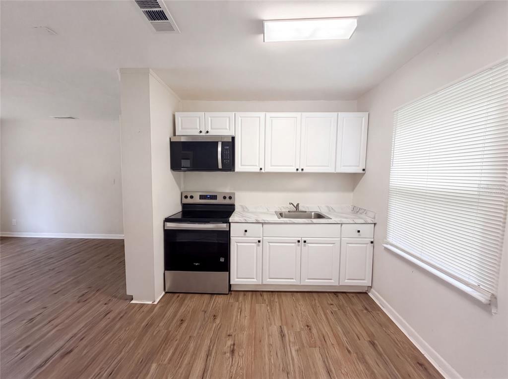 A kitchen features white cabinets, stainless steel appliances, and wood-look flooring — 706 FLANDERS AVENUE, DAYTONA BEACH, FL