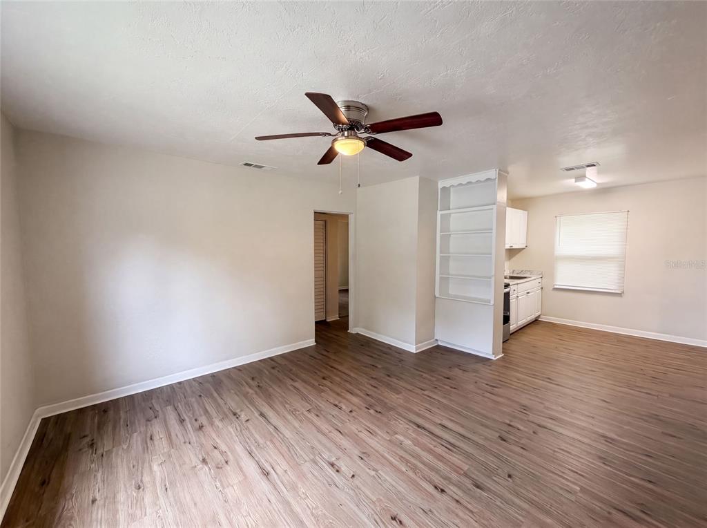 A living room with wood-look flooring, a ceiling fan, and an open view into a kitchen — 706 FLANDERS AVENUE, DAYTONA BEACH, FL