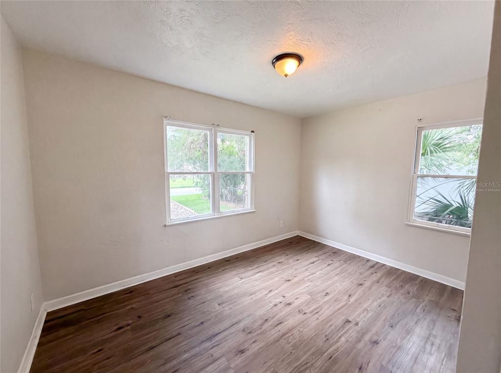 An empty bedroom features light-colored walls, wood-look flooring, two windows, and a ceiling light fixture — 706 FLANDERS AVENUE, DAYTONA BEACH, FL