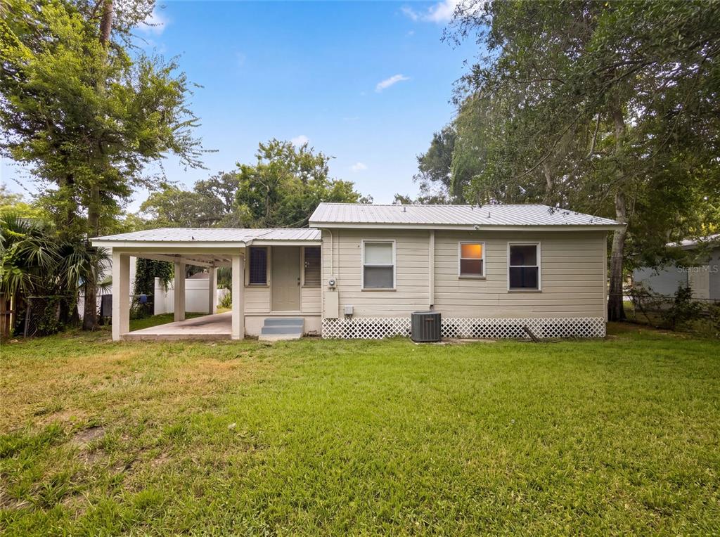 The exterior of a single-story house features light-colored siding, a metal roof, and a carport — 706 FLANDERS AVENUE, DAYTONA BEACH, FL