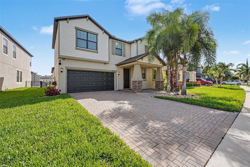 A two-story house features a paved driveway, a dark garage door, and a palm tree — 10032 SAGE CREEK DRIVE, SUN CITY CENTER, FL
