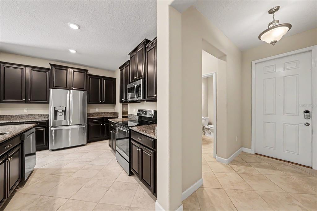 A kitchen with dark wood cabinets, stainless steel appliances, and tile flooring near an entryway — 10032 SAGE CREEK DRIVE, SUN CITY CENTER, FL