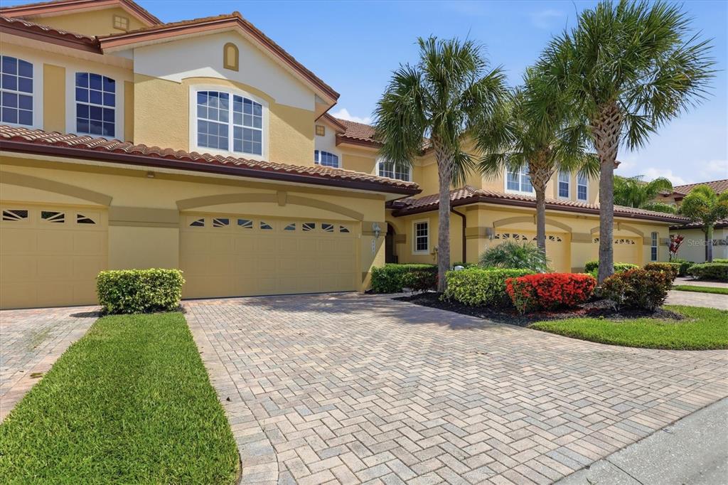 A two-story yellow stucco house with a paved driveway and palm trees in the front — 8434 MIRAMAR WAY, LAKEWOOD RANCH, FL