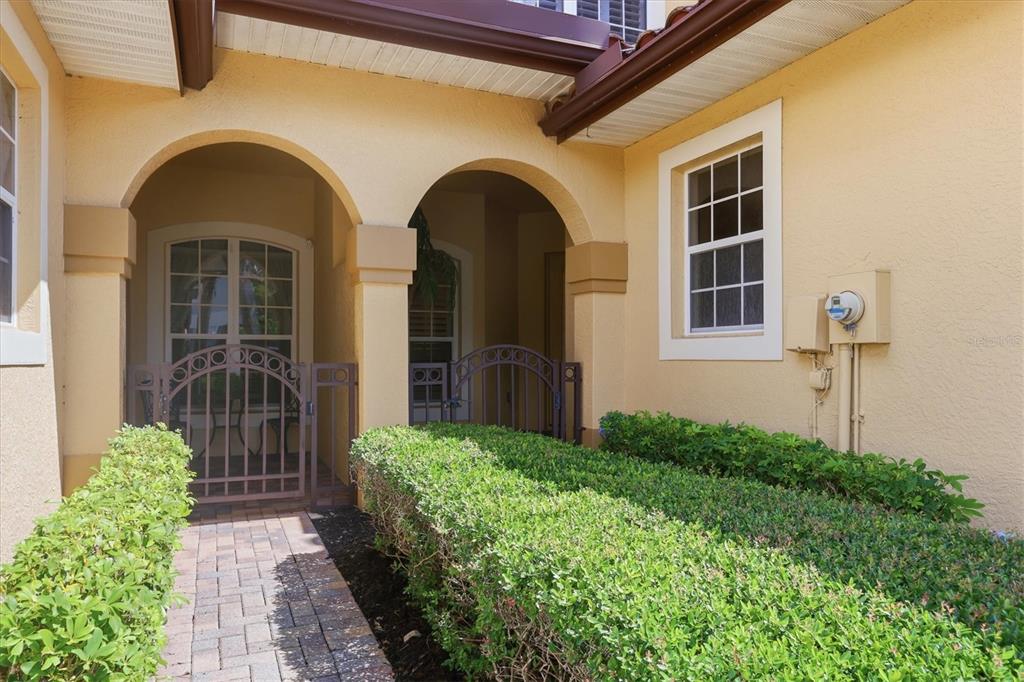 A paved walkway leads to a gated courtyard entrance with arched openings and stucco walls — 8434 MIRAMAR WAY, LAKEWOOD RANCH, FL