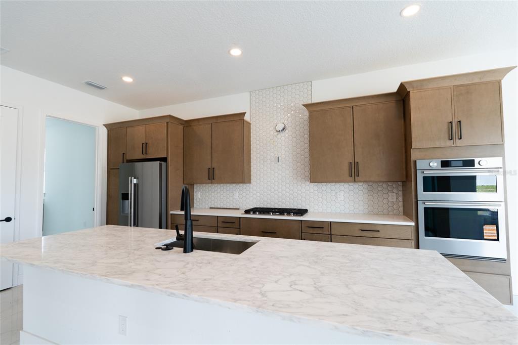 A kitchen features wood cabinets, white marble countertops, a central island, and stainless steel appliances — 659 MALDIVES TRAIL, SARASOTA, FL