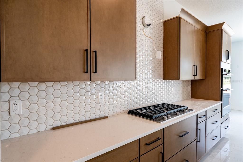 A kitchen features wood cabinets, white quartz countertops, and a white hexagonal tile backsplash — 659 MALDIVES TRAIL, SARASOTA, FL