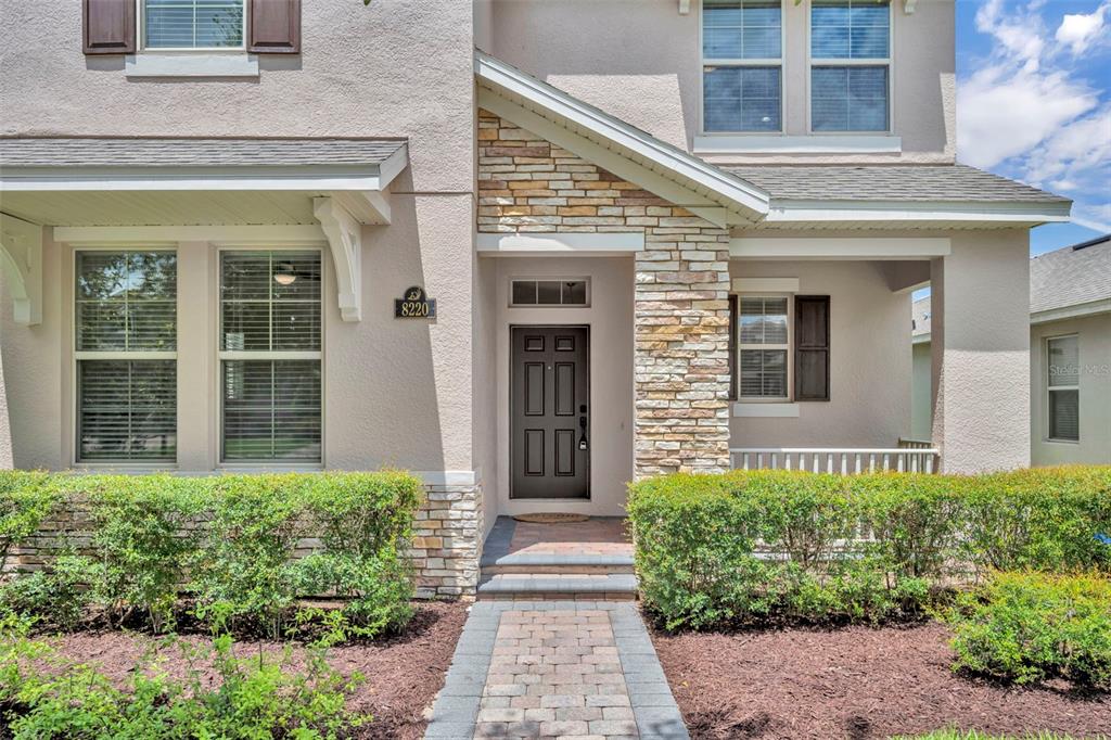 The exterior of a two-story home features a stone facade, a covered porch, and landscaping — 8220 BAYVIEW CROSSING DRIVE, WINTER GARDEN, FL