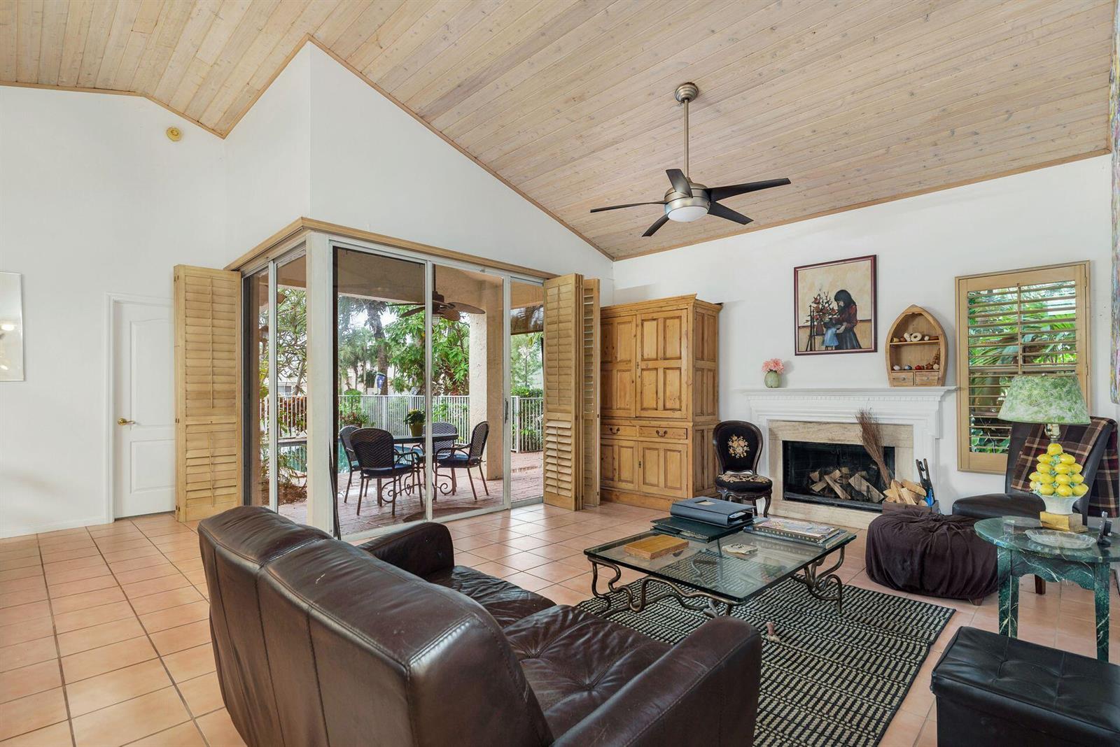 A living room features a vaulted wood ceiling, tile floors, a fireplace, and sliding glass doors — 9358 Heathridge Drive, West Palm Beach FL 33411, WEST PALM BEACH, FL
