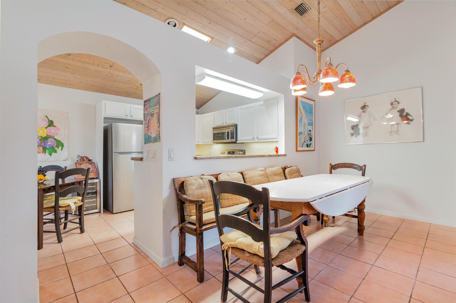 A dining area with a wooden bench, table, and chairs sits beside a kitchen pass-through — 9358 Heathridge Drive, West Palm Beach FL 33411, WEST PALM BEACH, FL