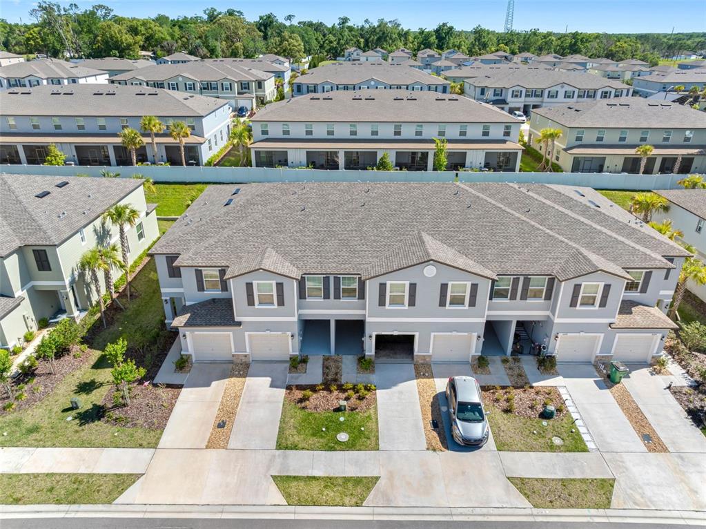 An aerial view shows a row of multi-story townhouses with gray siding and attached garages — 36488 WELL HILL WAY, ZEPHYRHILLS, FL