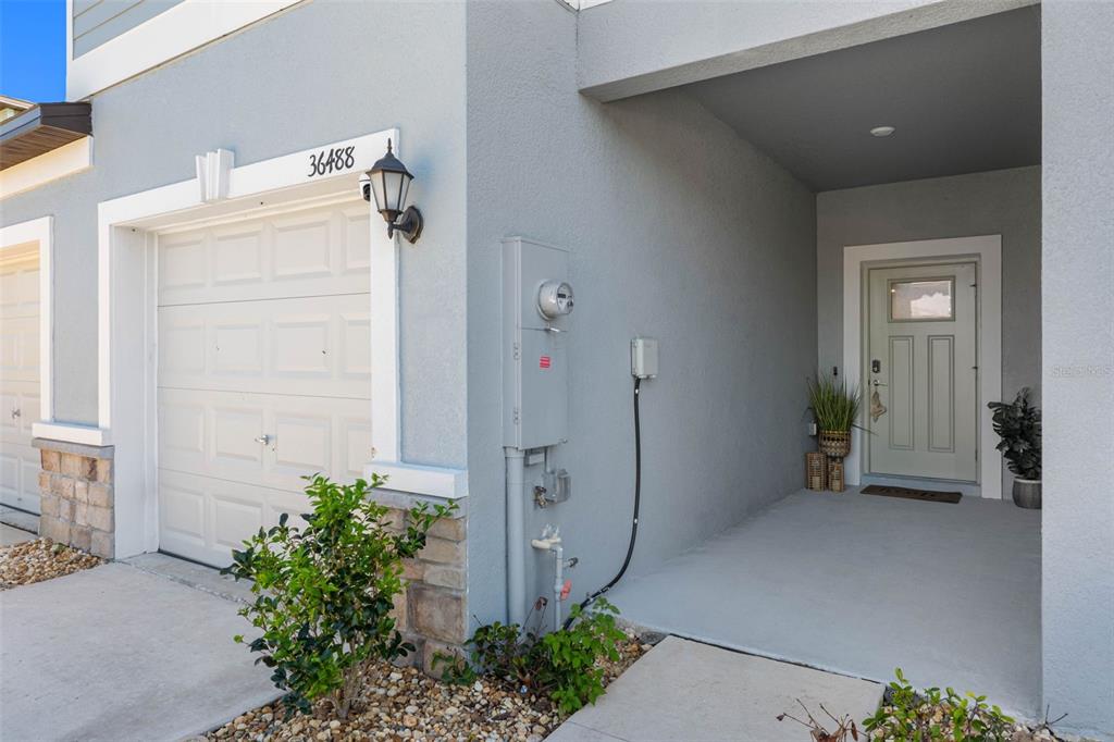 The exterior of a house shows a garage, a front entrance, and utility meters — 36488 WELL HILL WAY, ZEPHYRHILLS, FL