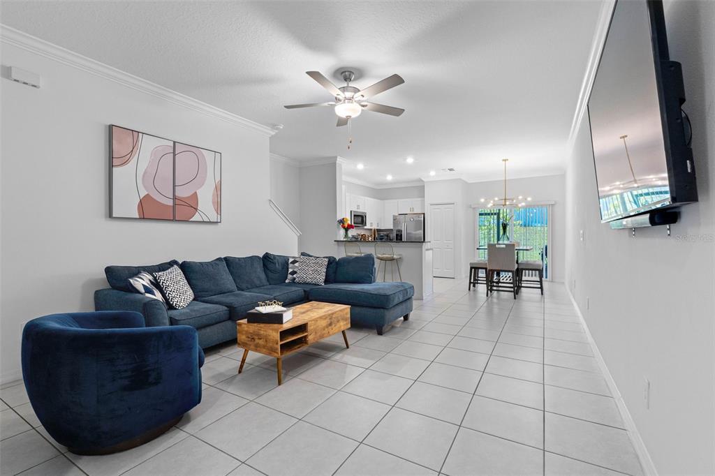 A living room with a blue sectional, a matching armchair, and an open-concept kitchen — 36488 WELL HILL WAY, ZEPHYRHILLS, FL
