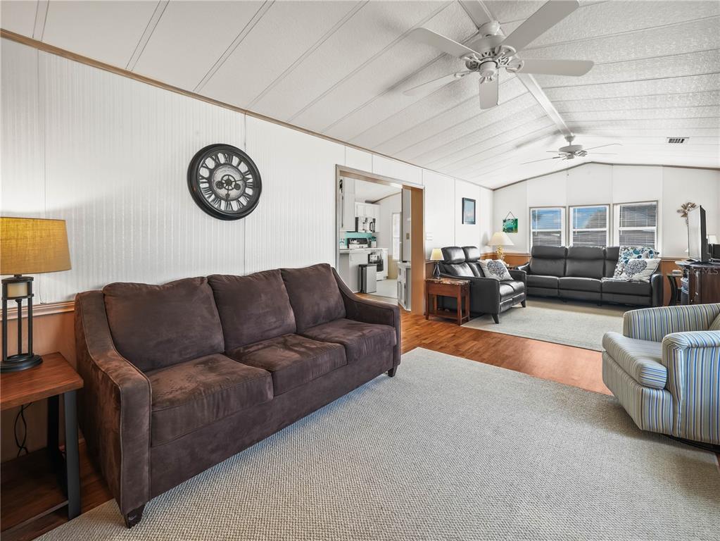 A living room with a brown sofa, striped armchair, and a view into the kitchen — 108 SILVERSIDES STREET, LAKE WALES, FL