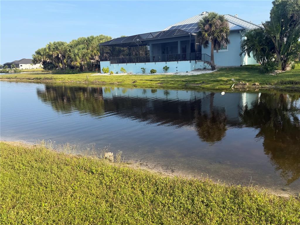 A light blue house with a screened-in porch sits behind a pond — 24336 SAN RAFAEL ROAD, PUNTA GORDA, FL
