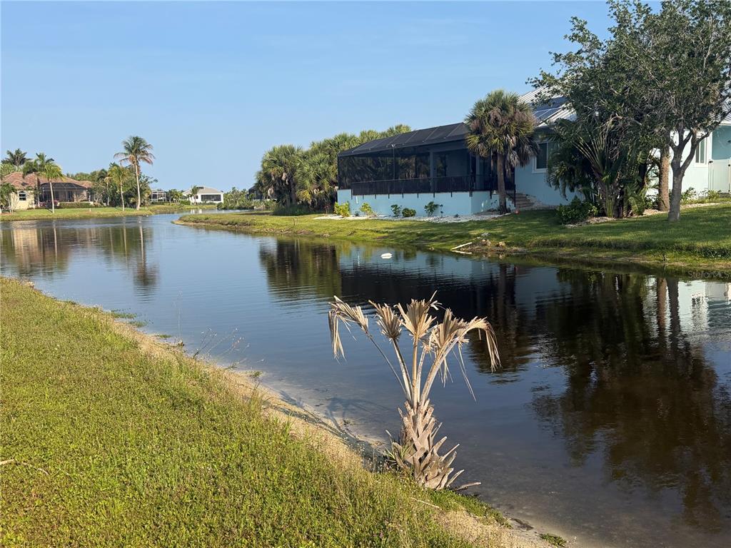 A view of a canal behind a house with a screened-in porch and palm trees — 24336 SAN RAFAEL ROAD, PUNTA GORDA, FL