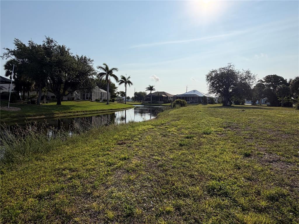 A grassy lot borders a narrow canal with palm trees and houses in the background — 24336 SAN RAFAEL ROAD, PUNTA GORDA, FL